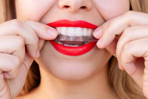 Close up of a young caucasian woman with red lips holding a 3d transparent teeth whitening strip